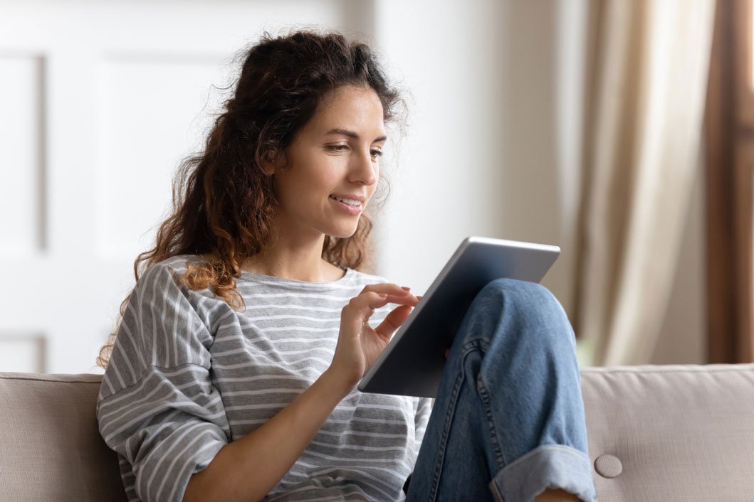 Woman sitting on couch reading news on tablet